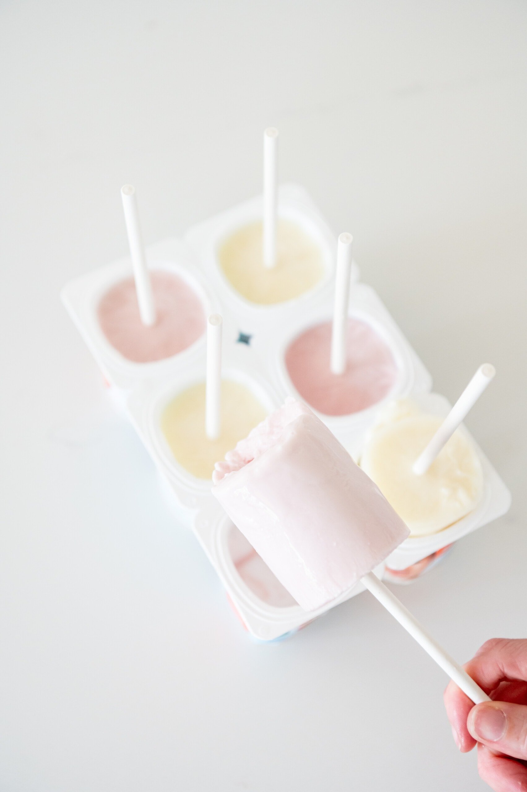 A frozen yogurt pop with a tray of yogurt cups with cookie sticks in the background.