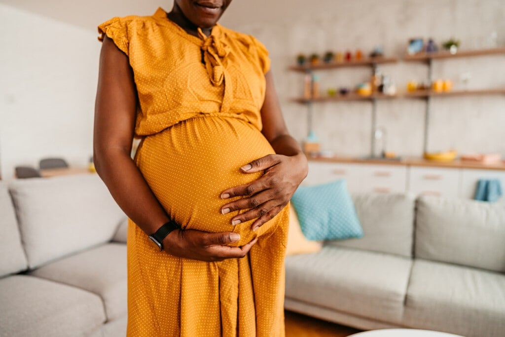 Portrait of beautiful pregnant black mother holding her pregnant belly at home. Close-up.