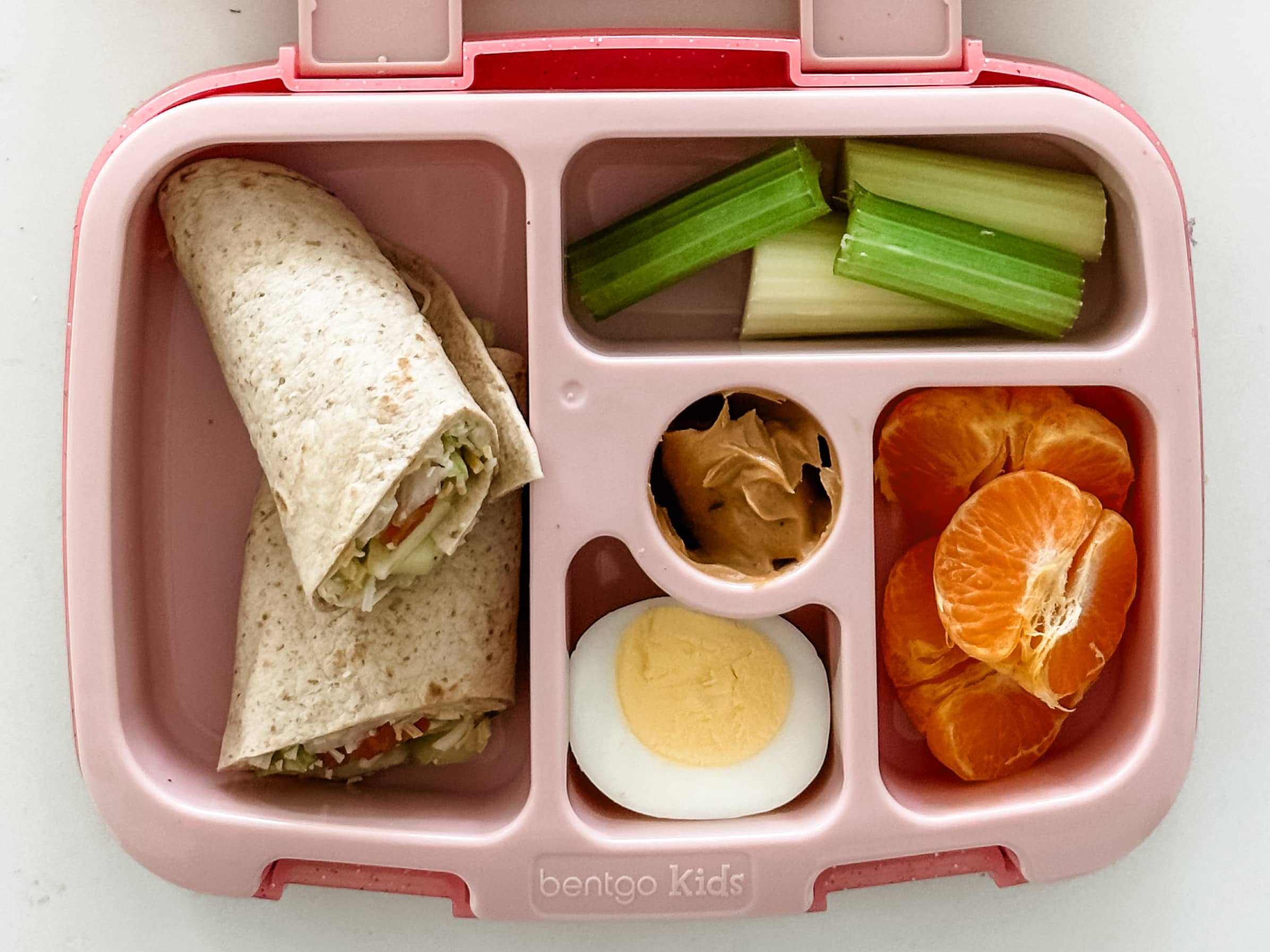 Kid's pink bento box with Hummus Wraps, hard boiled egg, clementine, and celery