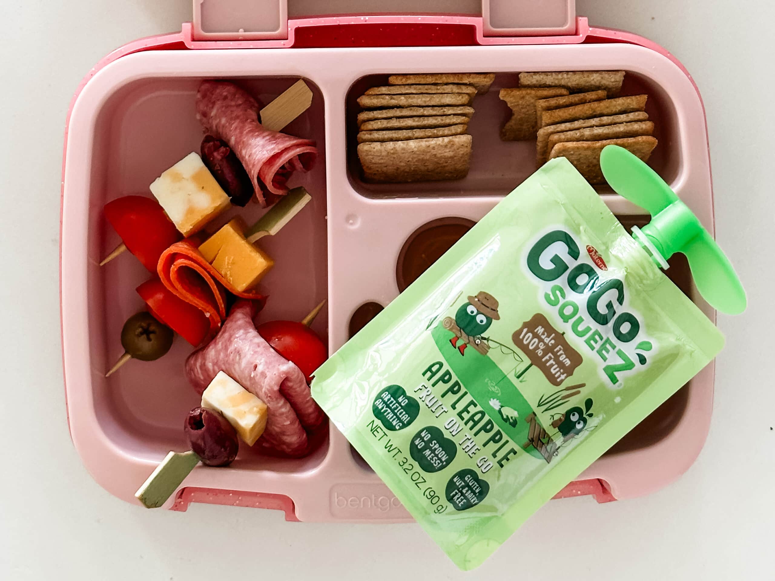 Kid's pink bento box with antipasto skewers, crackers, and apple sauce pouch