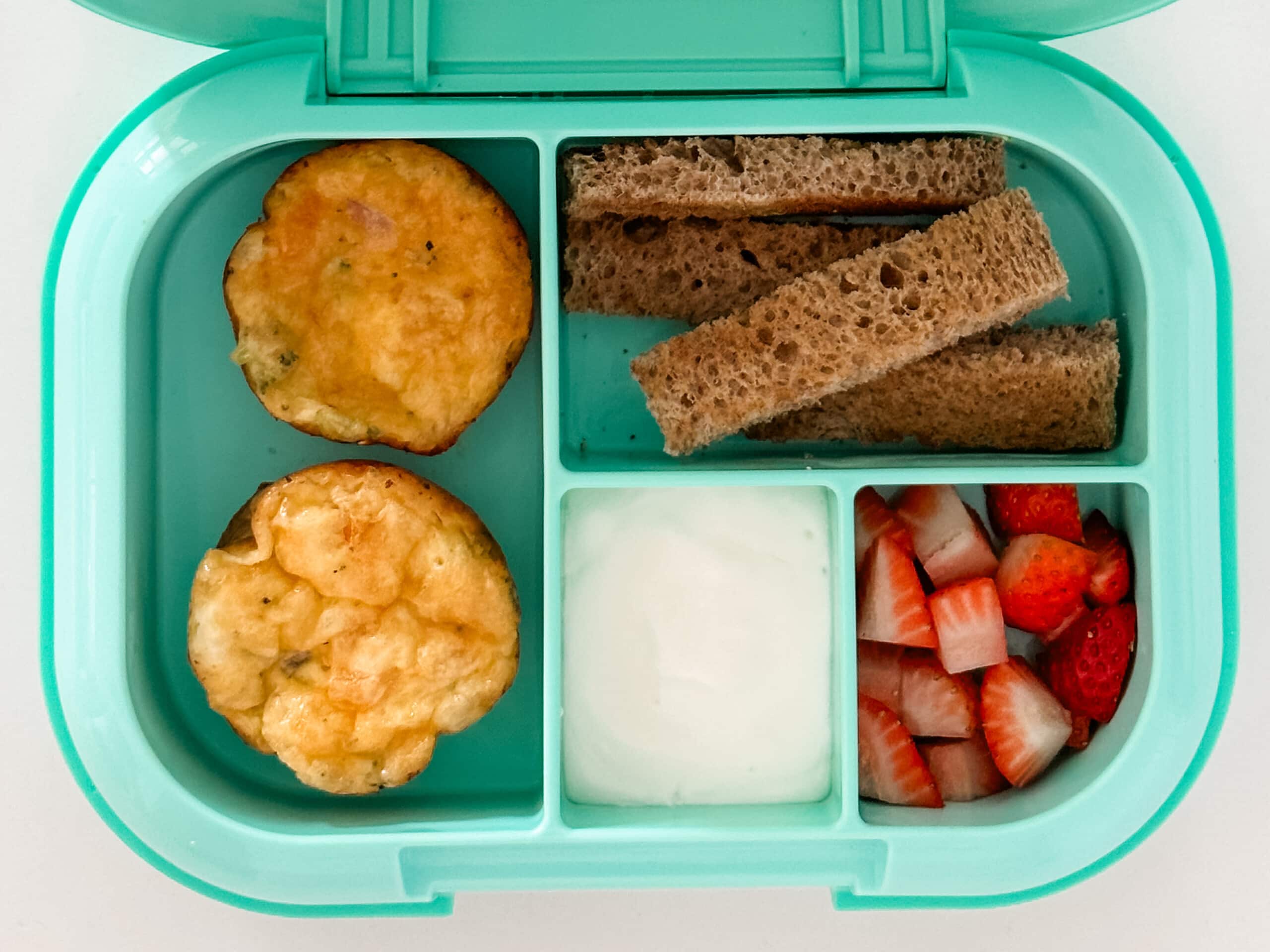 Mint green bento box for kids filled with egg muffins, toast, strawberries, and yogurt