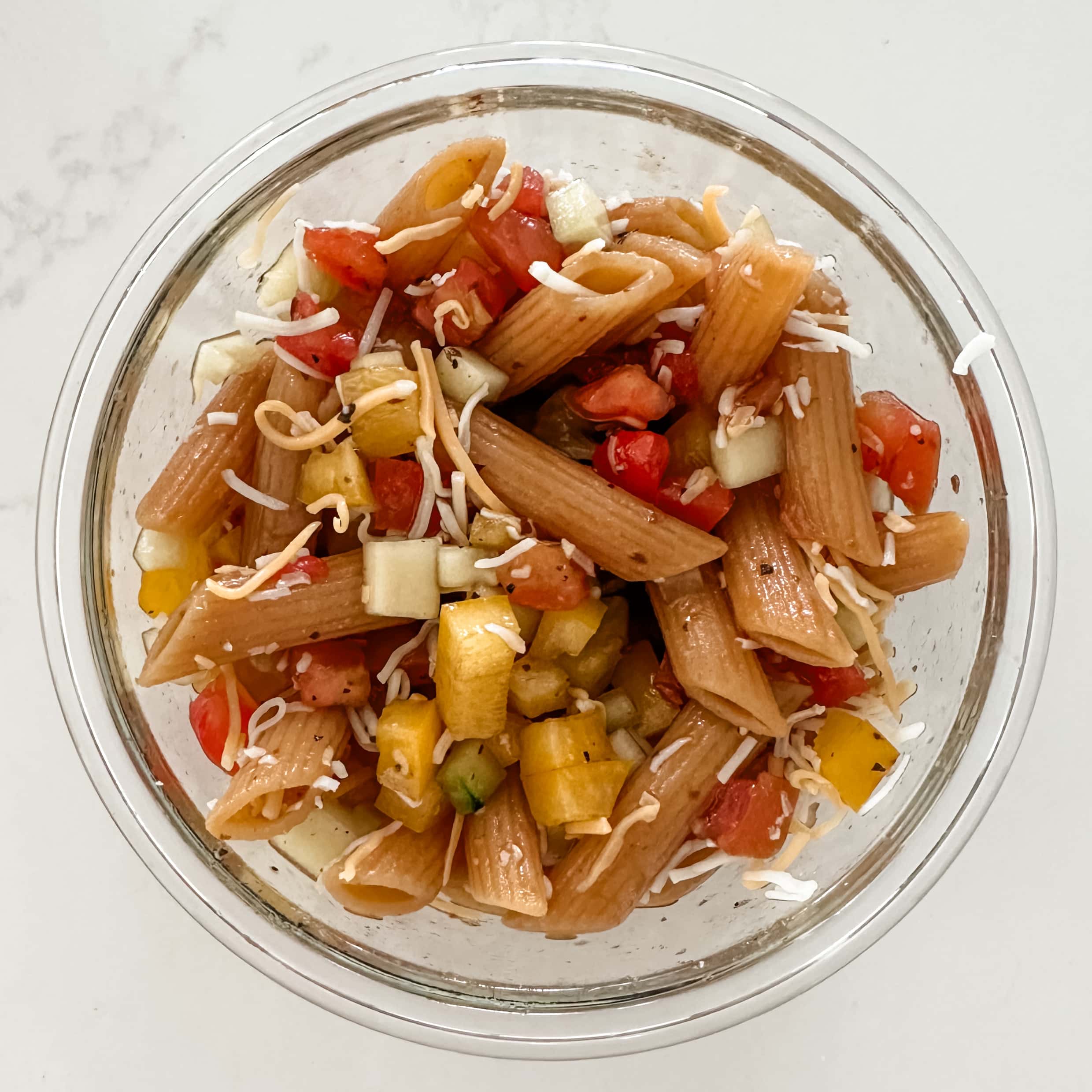 Clear round glass container filled with lentil pasta and veggies with a vinegarette.
