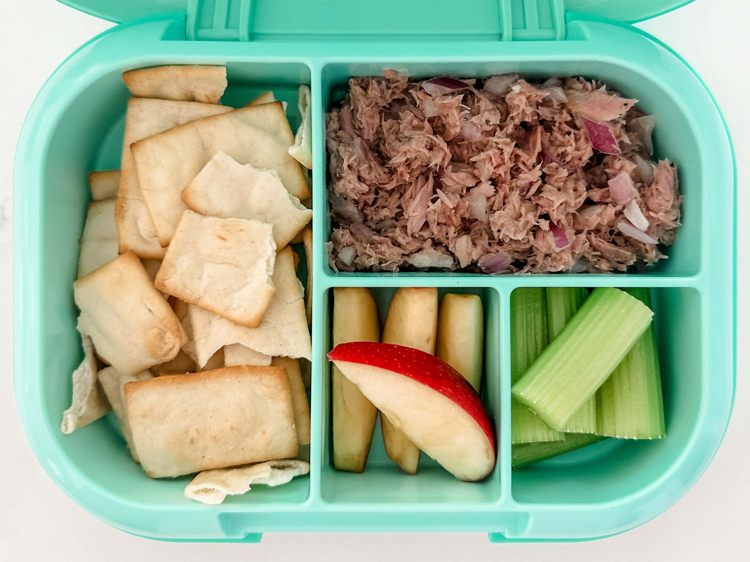 Mint green bento box for kids filled with tuna salad, pita chips, apple slices, celery sticks
