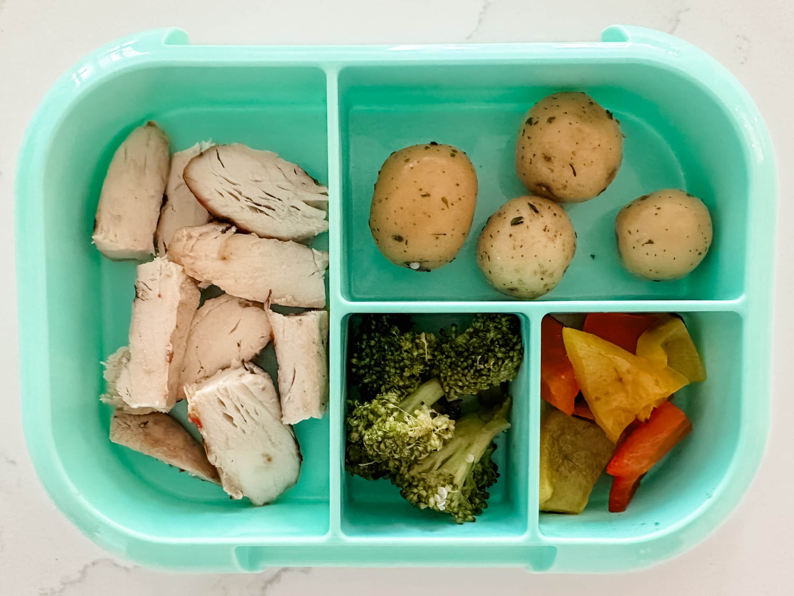 Mint green bento box for kids filled with chicken, potatoes, broccoli, and bell peppers.