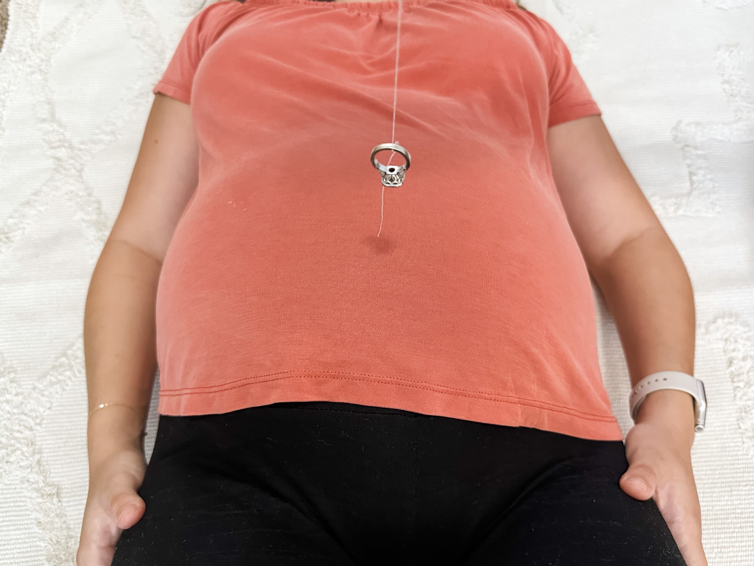 Pregnant woman laying down and there is a ring hanging on a string over her belly.