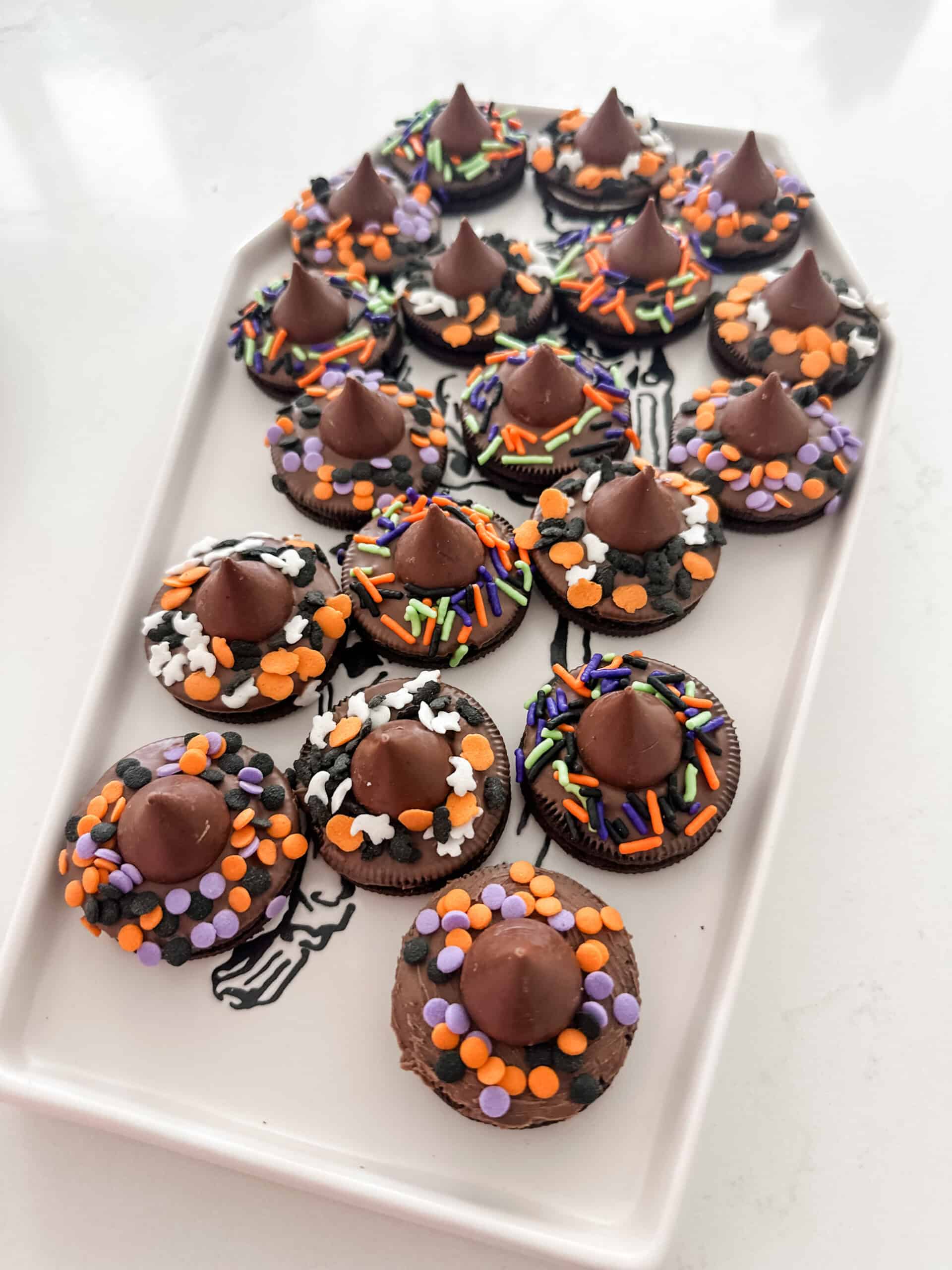 A rectangular plate features Halloween cookie treats, topped with chocolate kisses and colorful sprinkles in orange, purple, and black. Perfect for a kids Halloween party, the arrangement forms two neat rows on the plate.