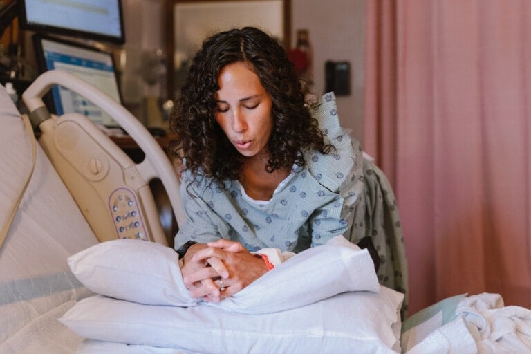 A beautiful multiracial pregnant woman rests agains pillows on a hospital bed in the delivery room and does breathing exercises during labor contractions.