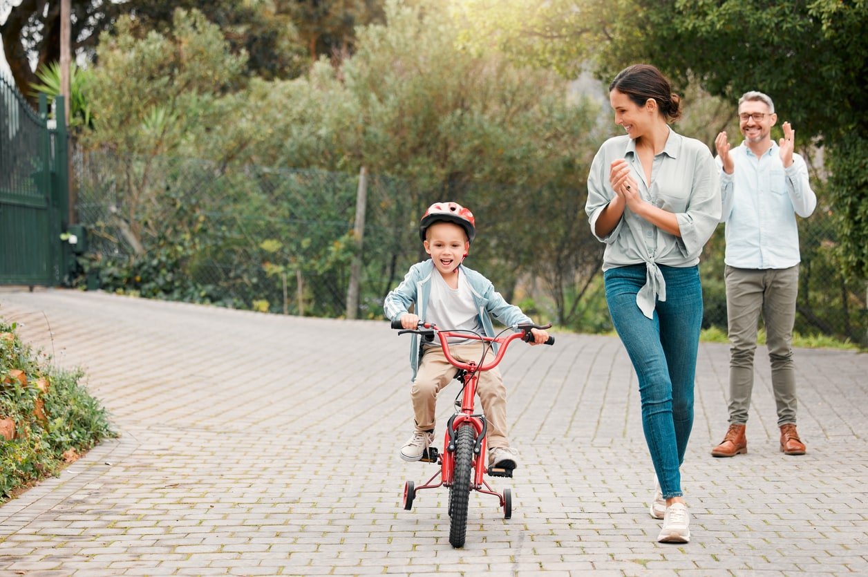 Shot of a little boy wearing a helmet and riding a bike outside with his mother