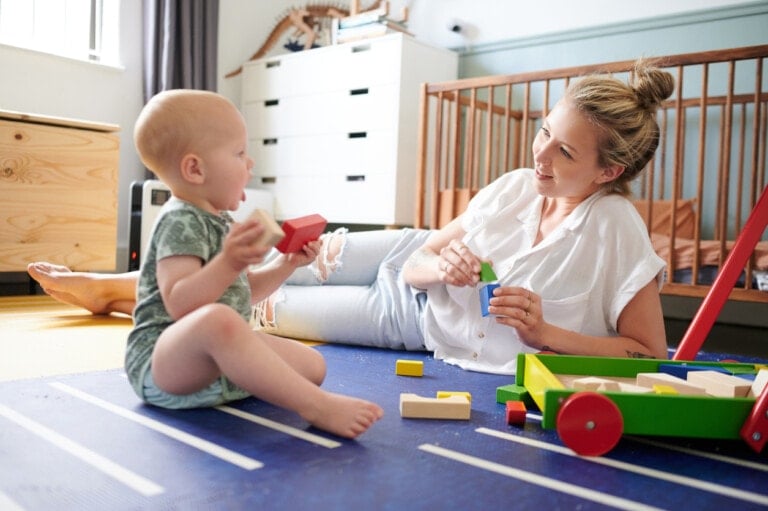 Young mom and young toddler playing in the nursery on the floor with blocks.