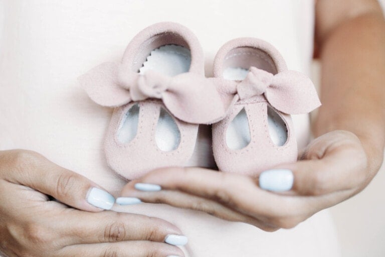 Small pink shoes for unborn baby on belly of pregnant woman.