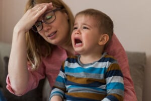 Tired, desperate mother is holding her two year old son, crying.Negative human emotion face. Upset toddler boy. Depression, stress or frustration.