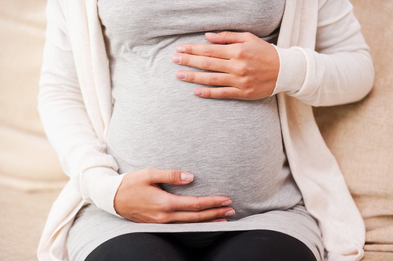 Close-up of young pregnant woman touching her abdomen while sitting on the couch
