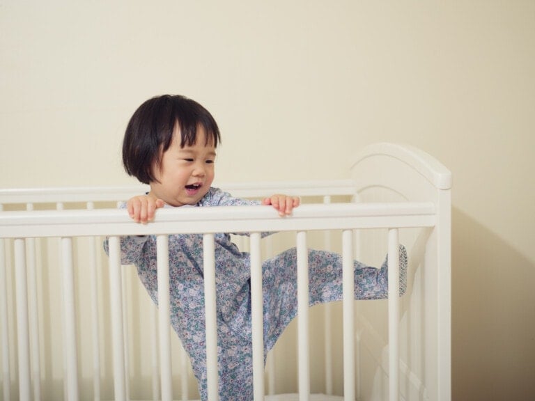 Young toddler girl in pajamas trying to climb out of her crib.