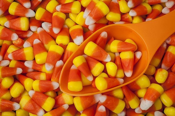 Candy corn and an orange spoon with some candy corn in it