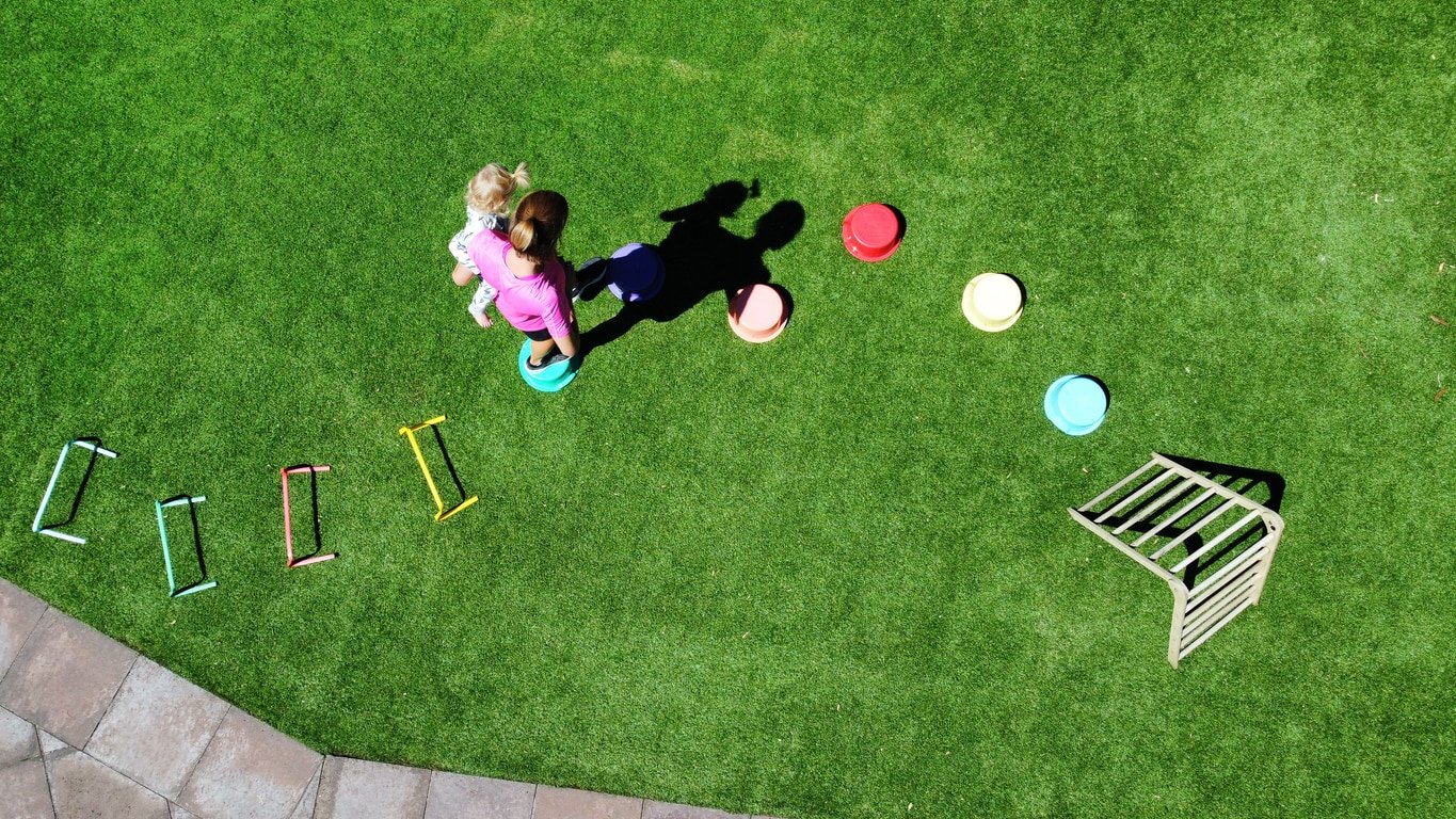 An obstacle course in the backyard on the grass or lawn with hurdles, steps and climbing frame for kids to get exercise and fitness outdoors. Young boy child, getting fit outside in the back garden on the green grass at home dressed up. Family fun and fitness in the yard. Abstract drone point of view.