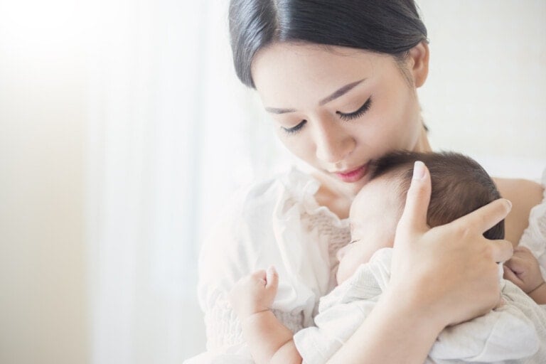 Close up portrait of beautiful young asian mother with her newborn baby, copy space with bed in the hospital background.