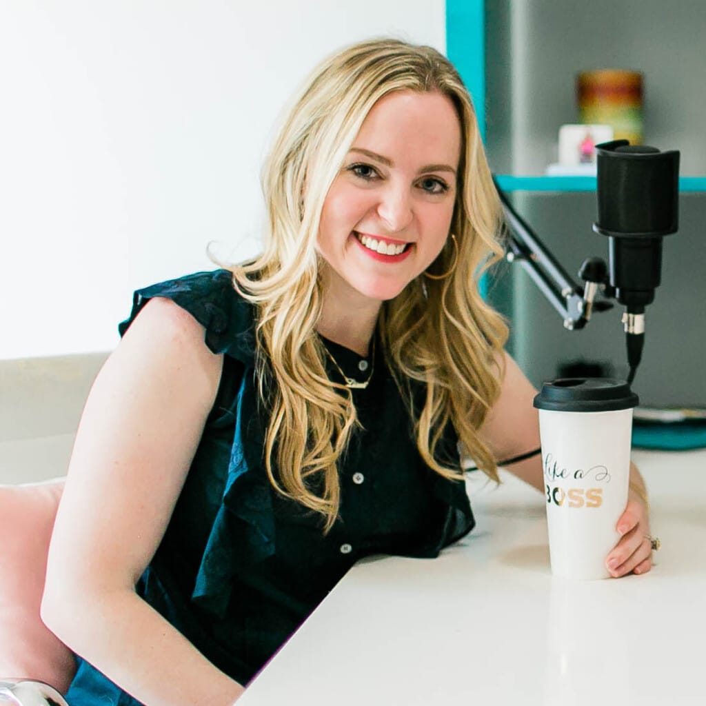 Nina Spears sitting at a desk with a coffee cup and podcast microphone smiling at the camera