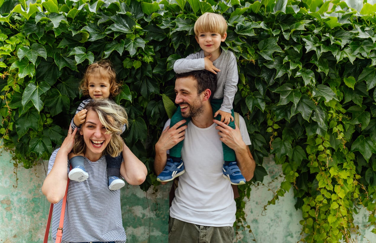 Portrait of happy family outdoors - mom and dad with their two kids on their shoulders