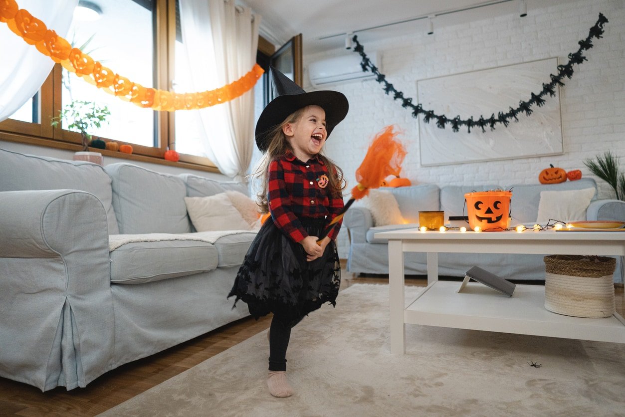 Caucasian toddler girl dressed as witch running with a broom, during Halloween