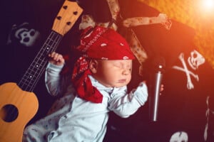 little baby in a rocker bandana lies with a guitar and a microphone on a blanket with skulls