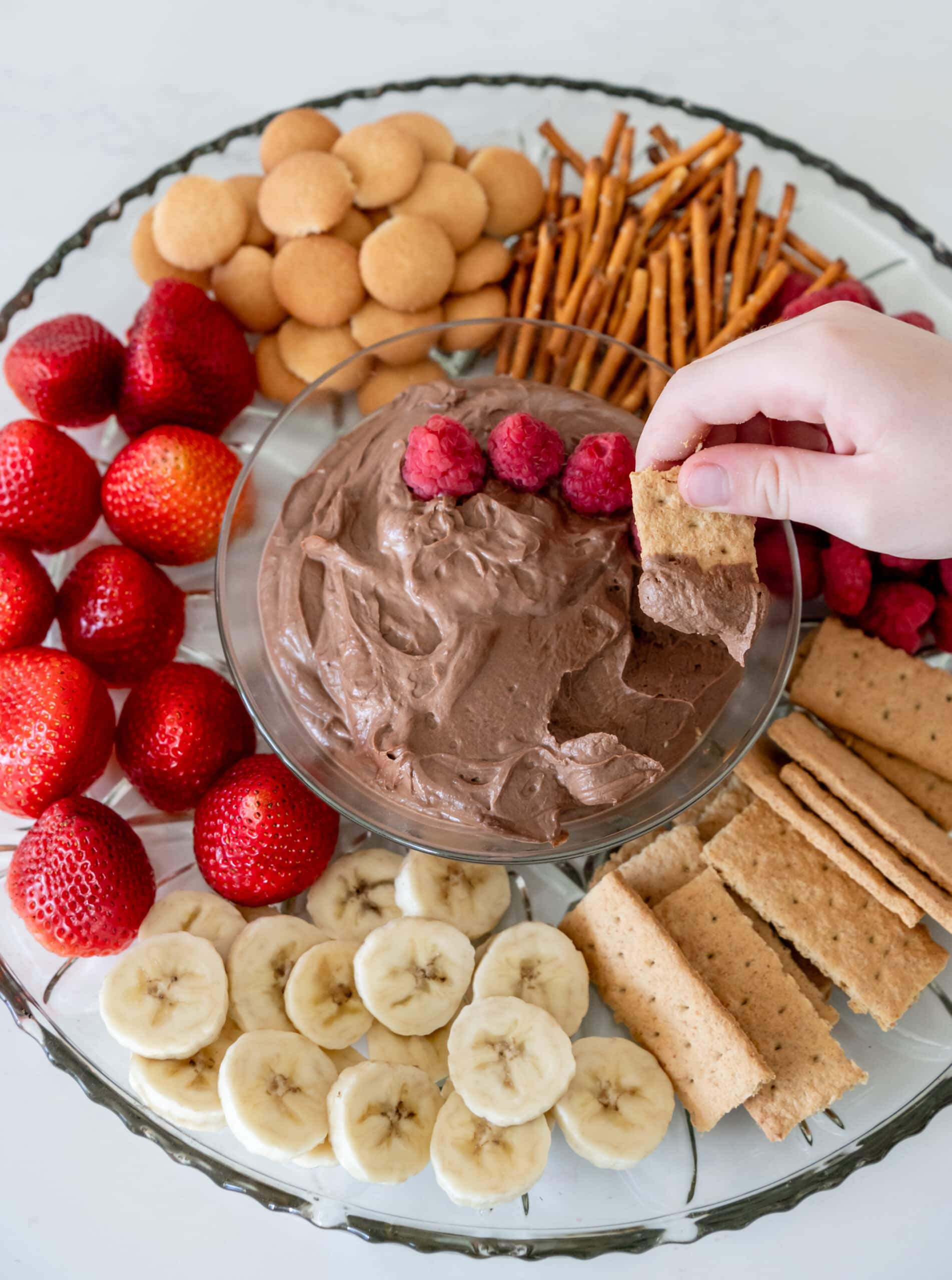 Little hand dipping a graham cracker into the chocolate peanut butter dip.