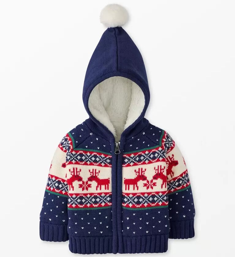 Navy blue hooded baby cardigan with a white pom-pom on the hood. This cute Christmas outfit features a knit pattern with red reindeer, snowflakes, small white hearts, and a zip closure down the front—perfect for cozy baby boy clothes this festive season.