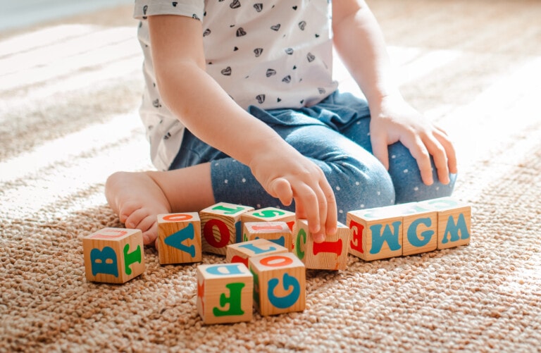 3 year old child plays with wooden cubes with colorful letters on the floor in the room a little girl is building a tower at home or in the kindergarten. Educational toys for young children.