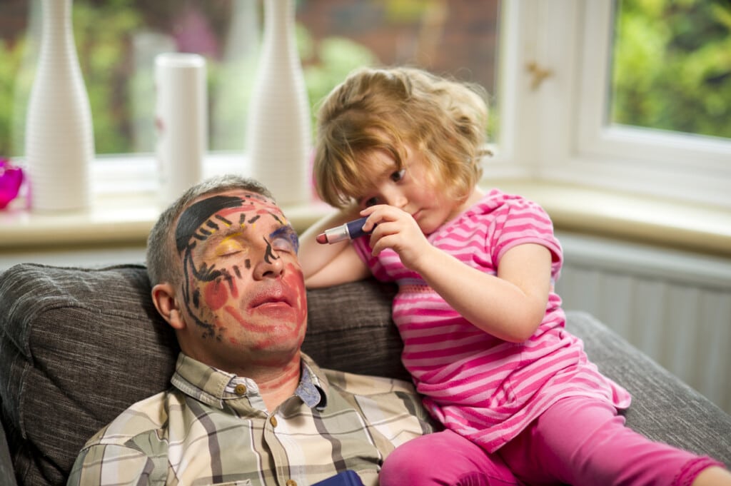 little girl has fun with a sleeping father and colors on his face