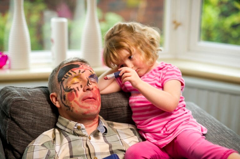 little girl has fun with a sleeping father and colors on his face