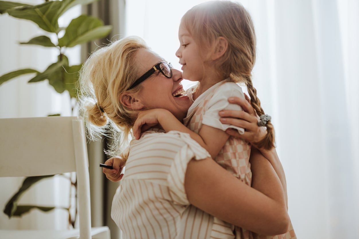 Cheerful little girl hugging her loving mother in the living room.