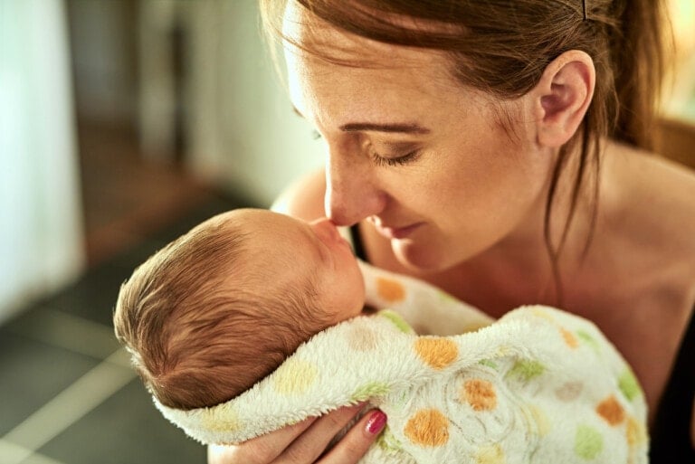 Closeup of a cheerful young mother holding her infant son in a blanket in her arms at home