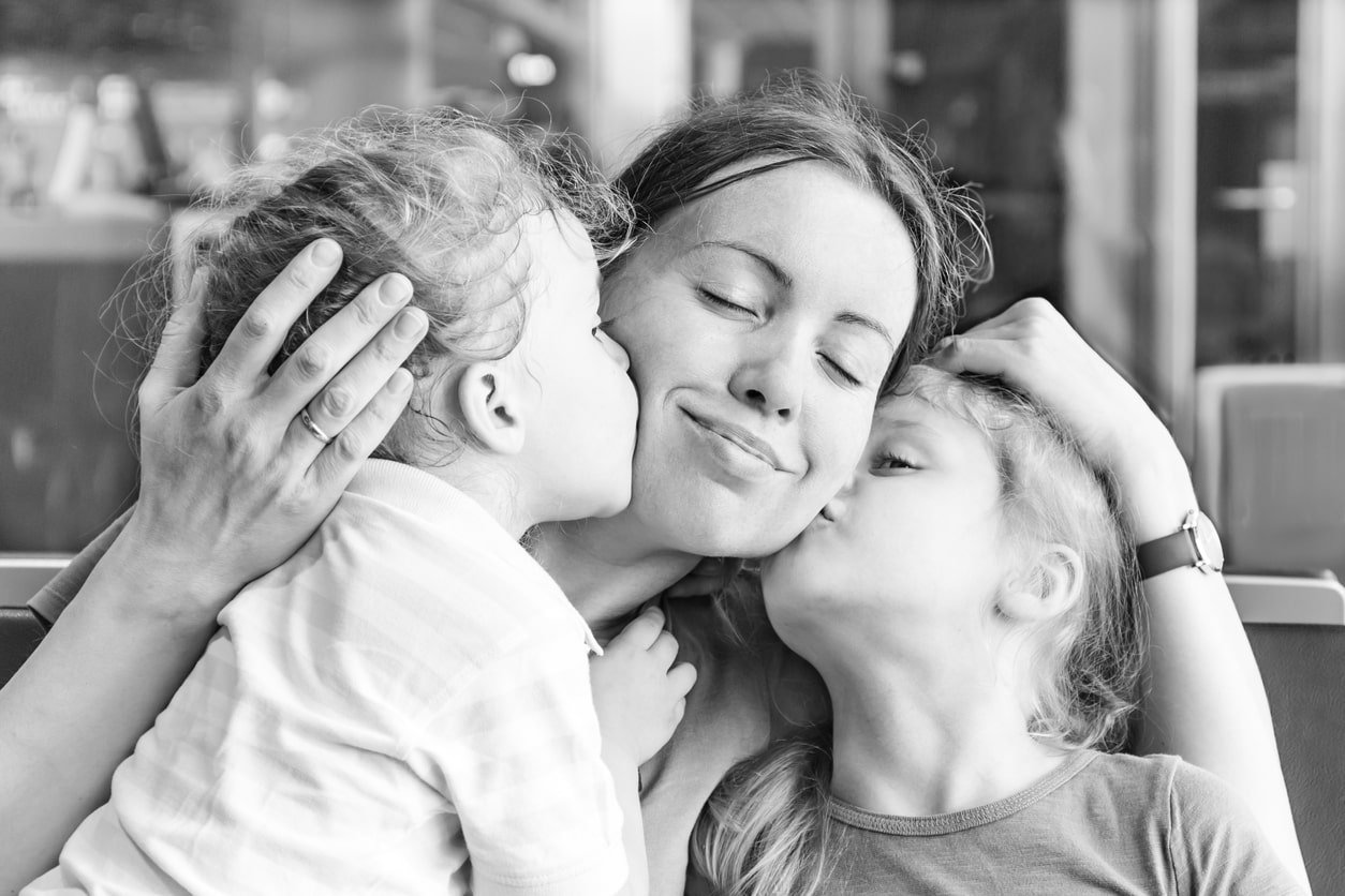 Two daughters kissing their happy mother on the cheeks