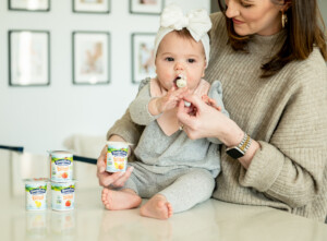 Baby eating yogurt on counter with her mom