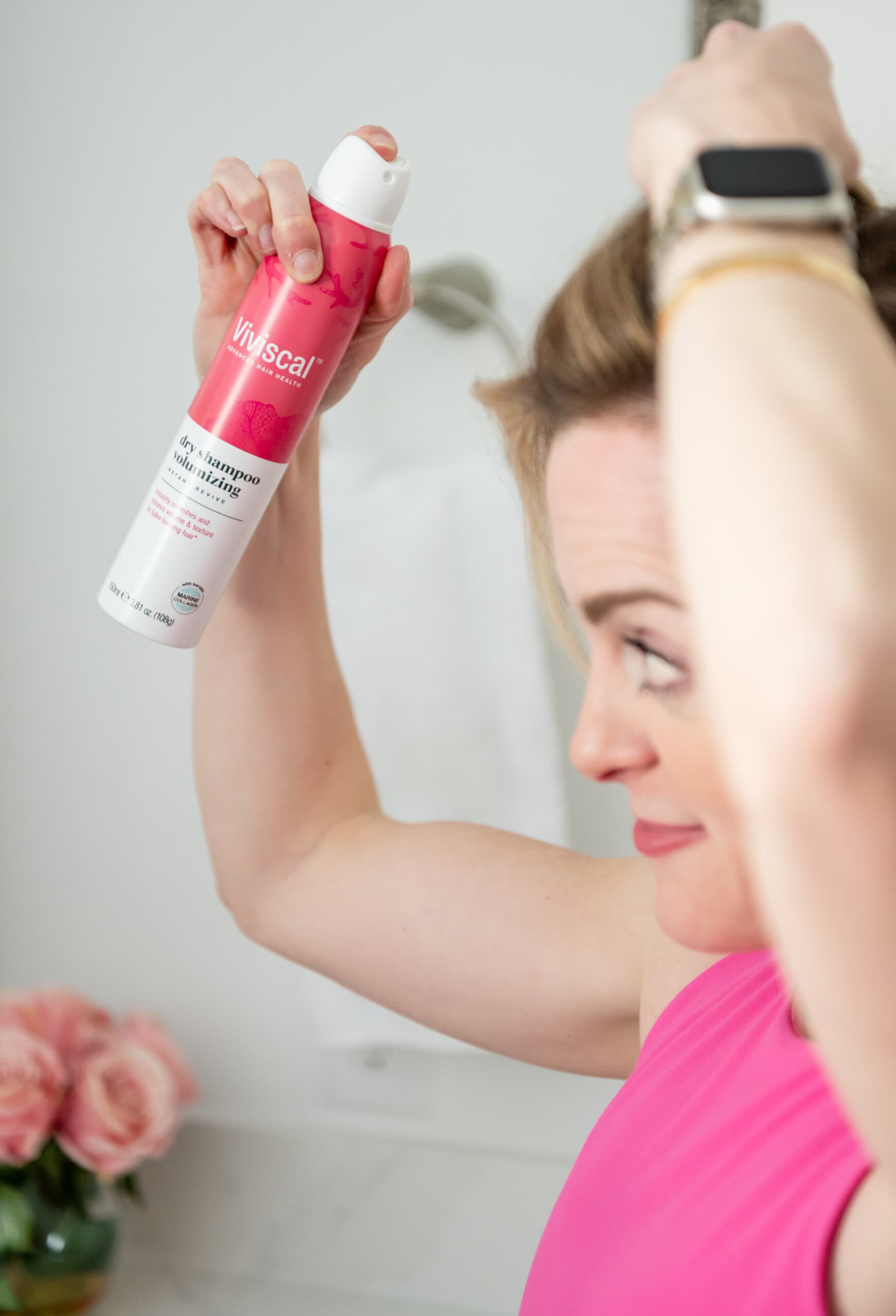 Woman spraying Viviscal dry shampoo into her hair and scalp