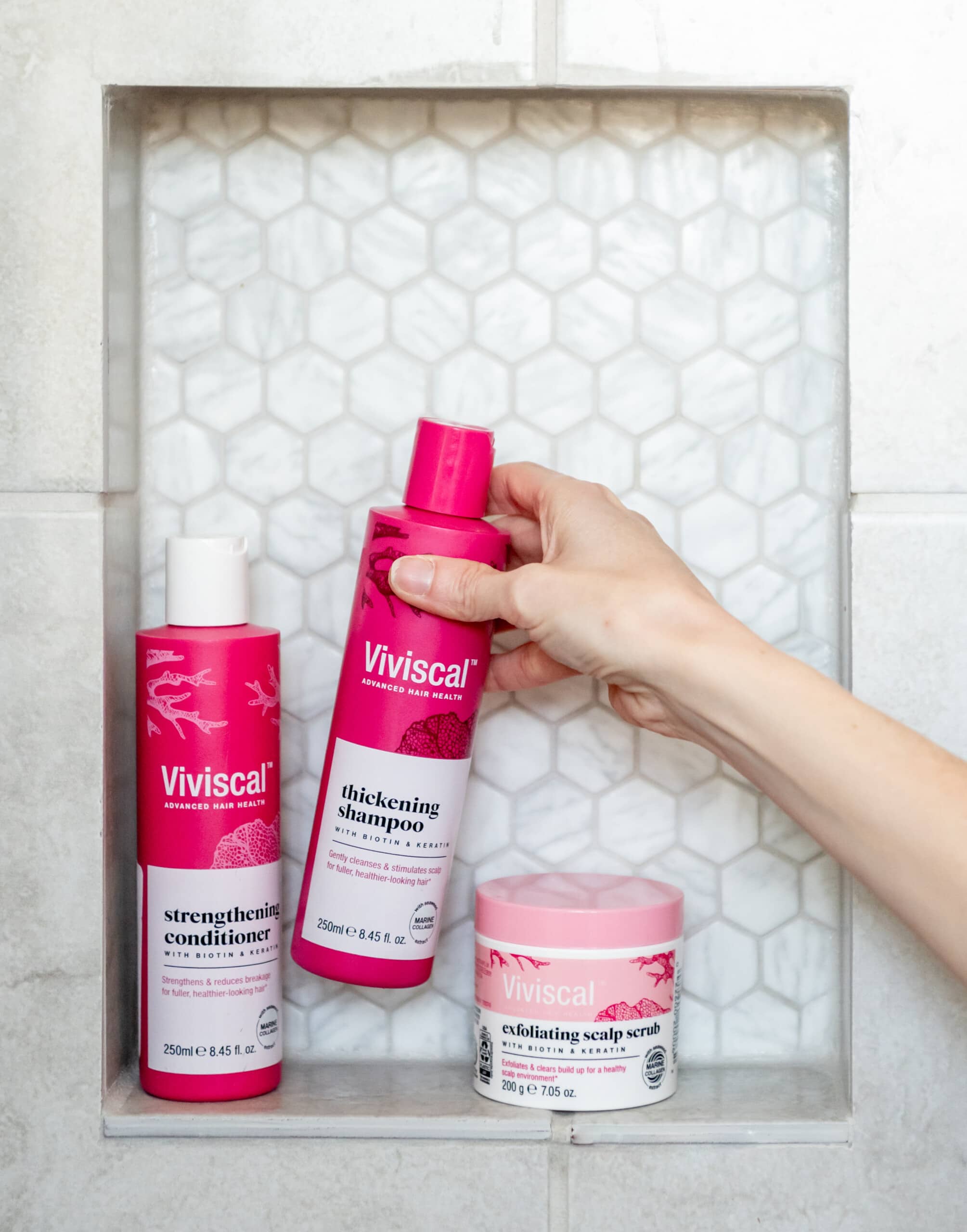 Viviscal shampoo, conditioner, and scalp scrub in the bathroom ledge