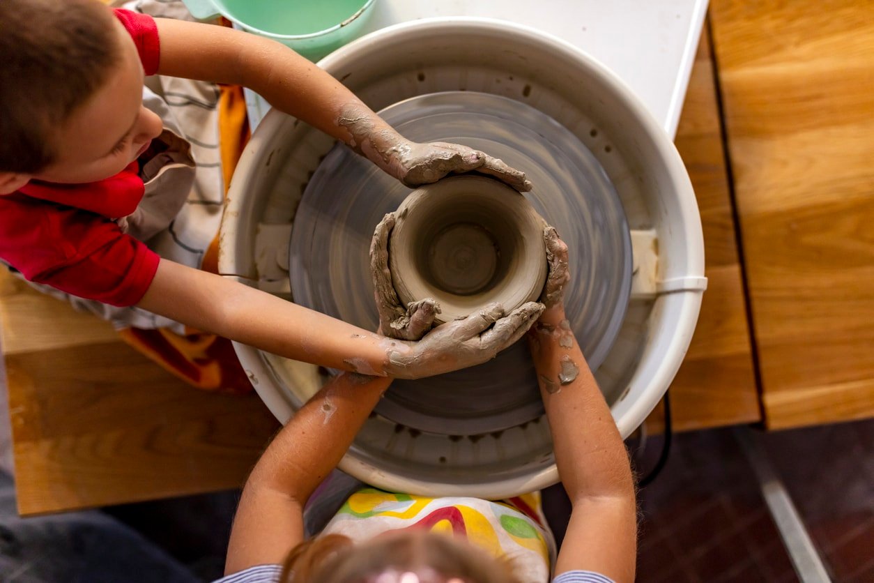 Top view of a two kids hands making jugs in pottery-wheel.