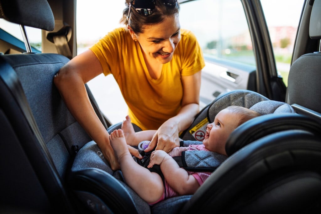 Mid adult mother putting baby girl in car seat