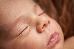Newborn baby sleeping on a brown fur with the facial details in selective focus.