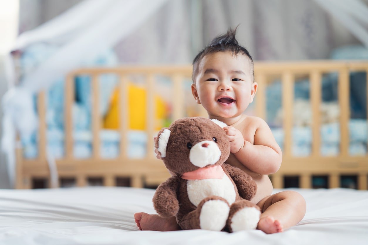 Asian baby sit with teddy bear on their bed in bedroom