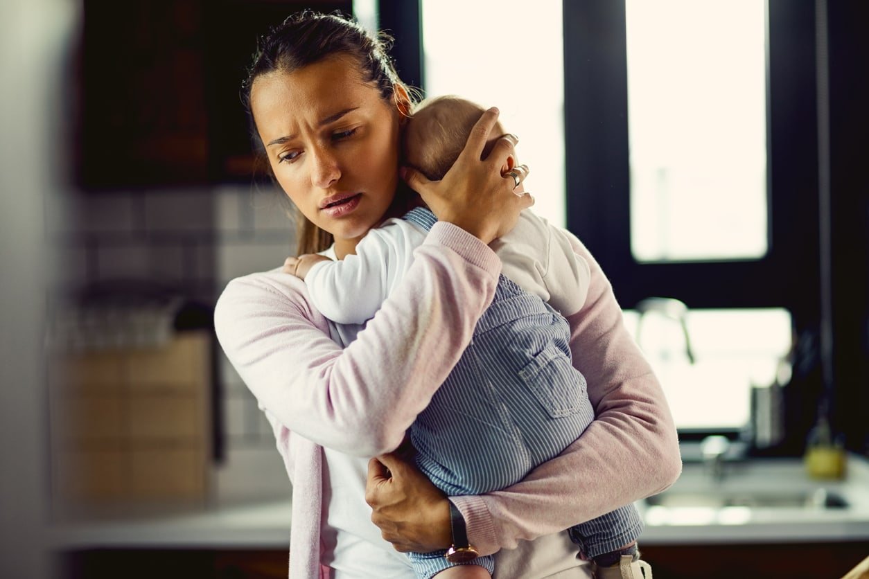 Young mother holding her baby son and consoling him at home.