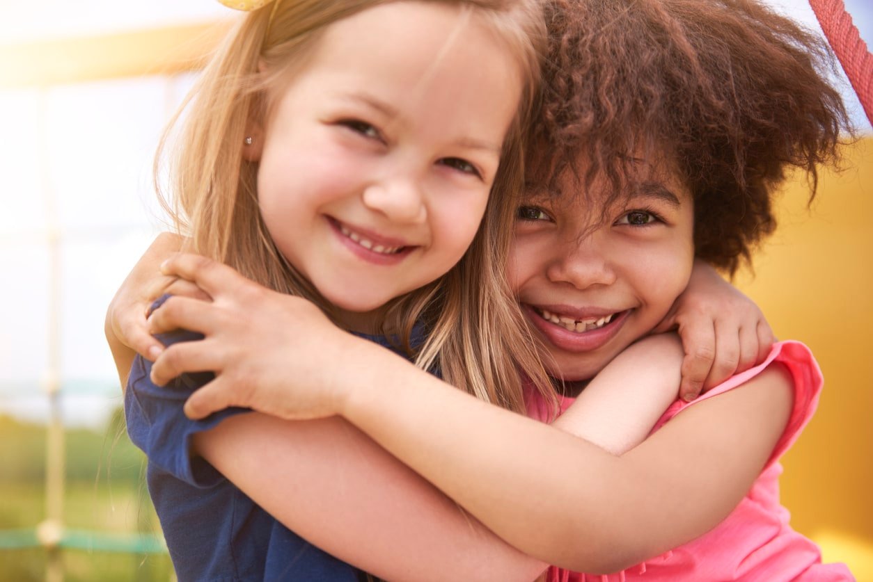 Two little girls giving each other a hug while they are playing outside.