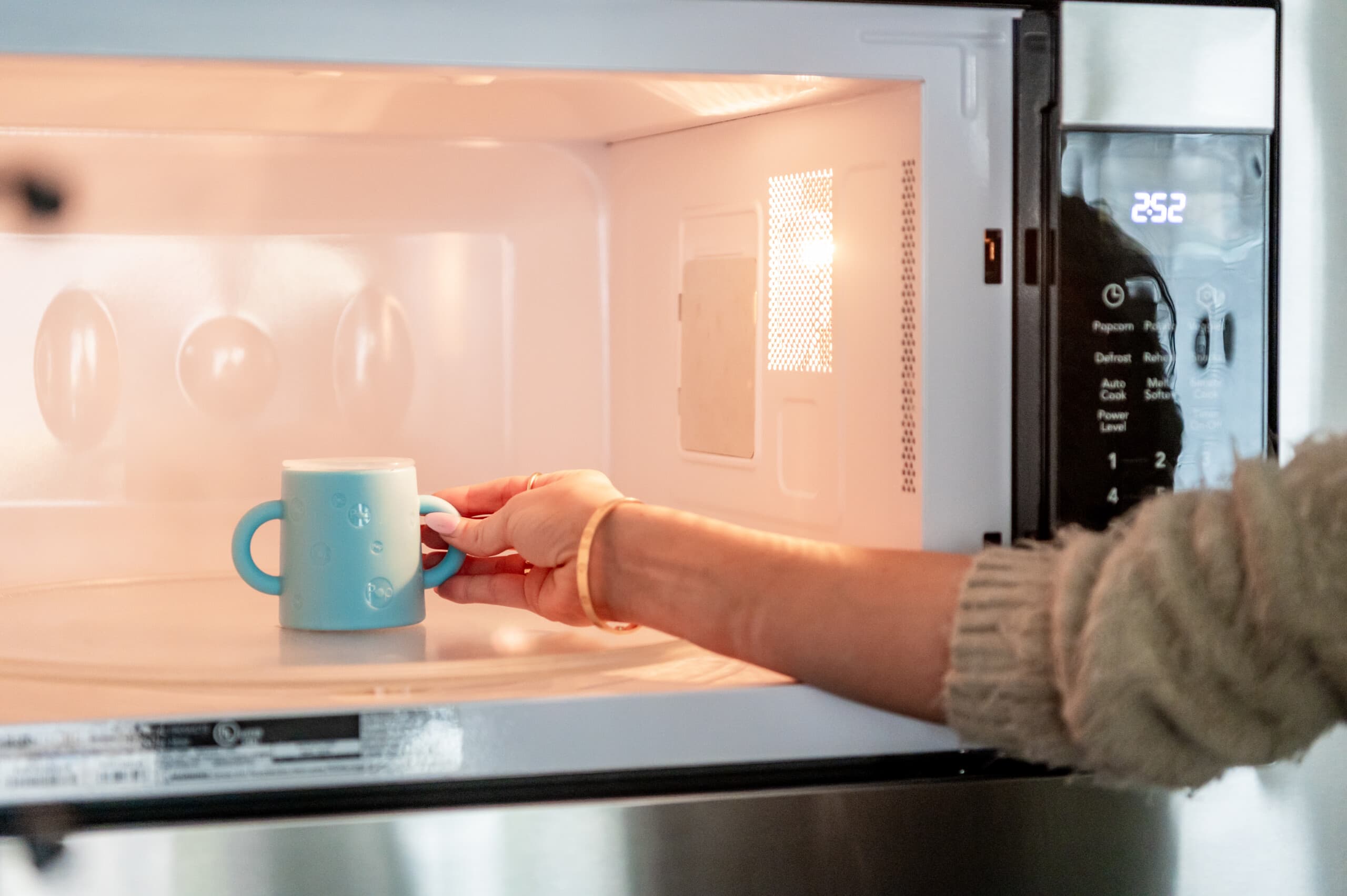 Woman's hand putting the PopYum silicone cup in the microwave.
