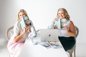 Jennifer and Laura from Moms on Call looking at their book, sitting at a desk recording their podcast.