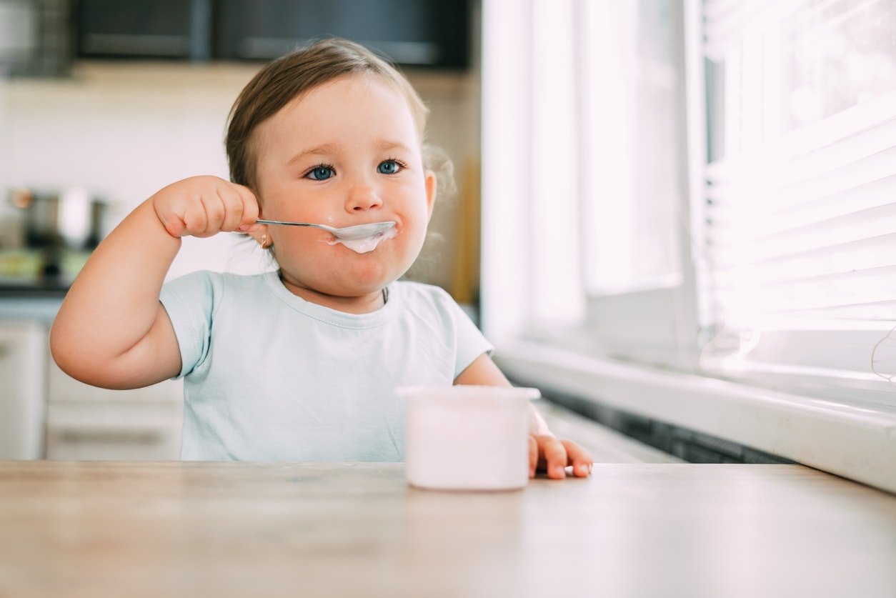 Little girl in the afternoon in the kitchen eating yogurt is very cute