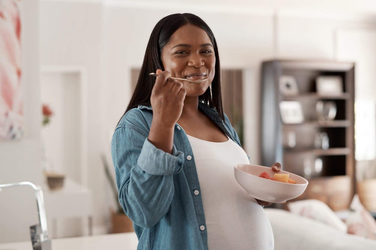 Portrait of a pregnant woman eating a bowl of fruit at home