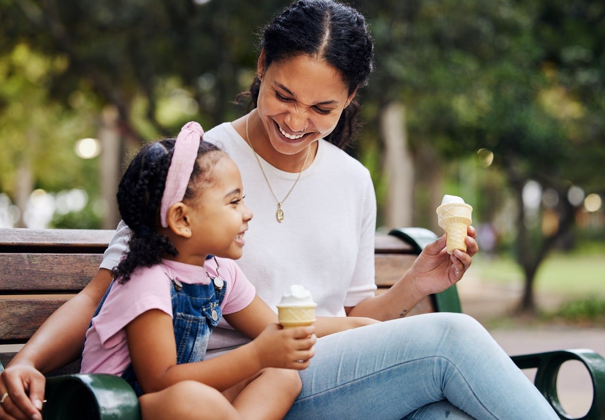 Summer, park and ice cream with a mother and daughter bonding together while sitting on a bench outdoor in nature. Black family, children and garden with a woman and girl enjoying a sweet snack