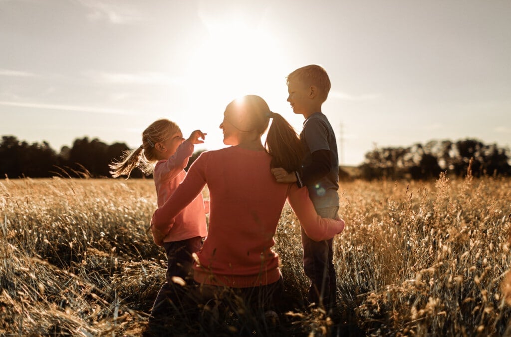 Mother and her two children boy and girl relaxing in nature grass field watching the sunset.