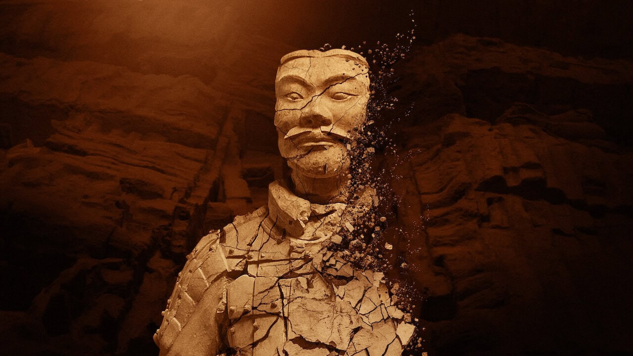 Mysteries of the Terracotta Warriors. A detailed stone statue of a mustachioed man is partially crumbling, with fragments breaking away from the right side. The dark background accentuates the intricate features and weathered texture, making it feel like you're watching a scene unfold in an evocative what-to-watch drama.