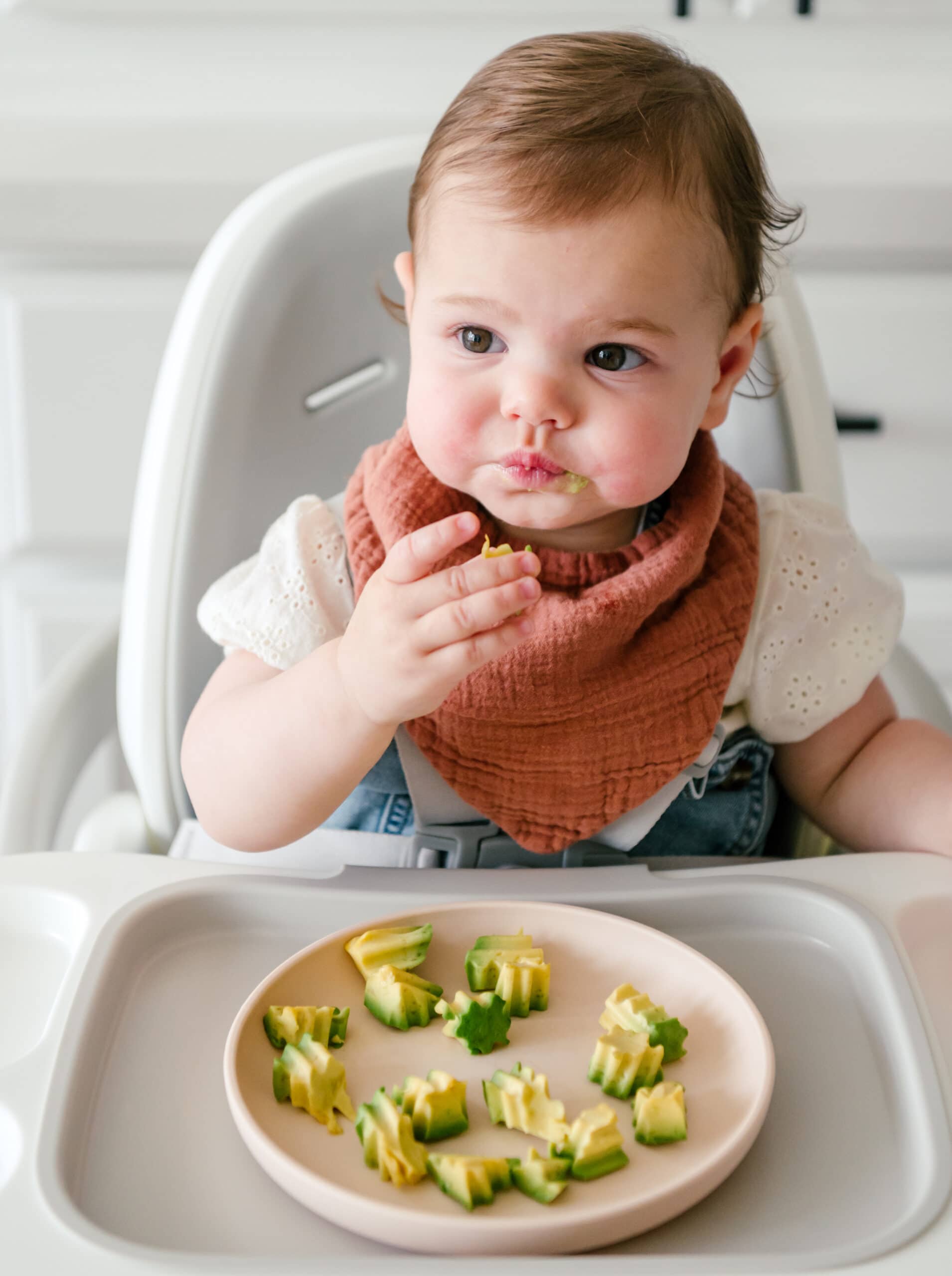 Baby eating avocado while sitting in high chair
