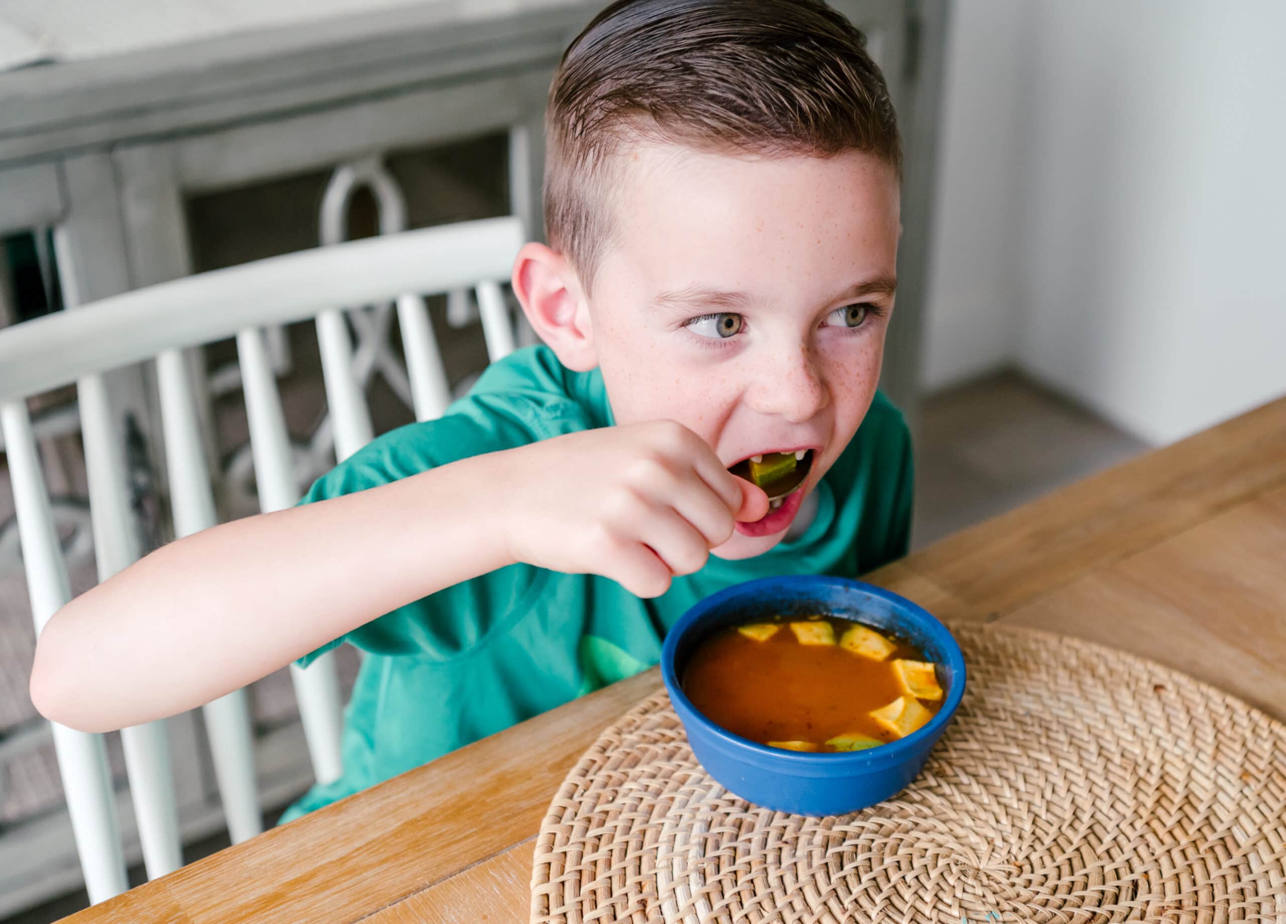 young boy sitting down eating a bowl of soup
